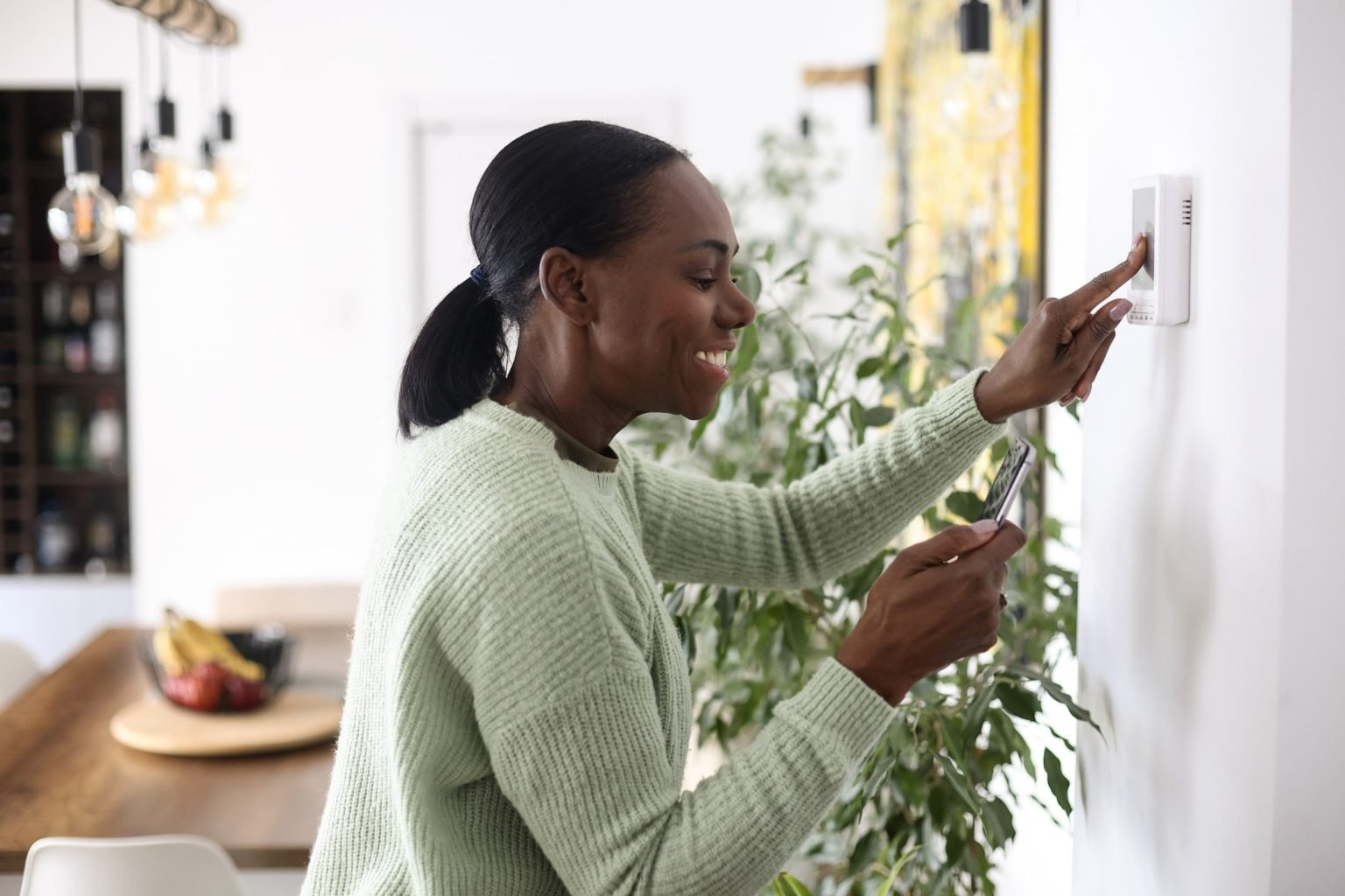 Woman adjusting a thermostat in a bright home